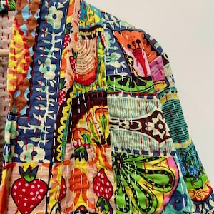 May include: A colorful patchwork jacket with a variety of patterns, including strawberries, flowers, and abstract shapes. The jacket features a mix of blue, red, yellow, and green hues, with white stitching throughout. The garment is made of a soft, quilted fabric.