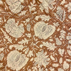 Op de afbeelding: Close-up van een bruin en cr&egrave;mekleurig bloemenpatroon textiel. Het ontwerp toont grote gestileerde bloemen en bladeren met ingewikkelde details. De stof is gestikt met een contrasterend garen, waardoor een gewatteerd effect ontstaat. De algehele esthetiek is vintage en handgemaakt.
