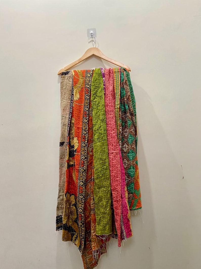 May include: A colorful, patchwork quilt hanging on a wooden hanger. The quilt features various patterned fabrics in shades of orange, green, pink, and brown. The quilt is made of stitched fabric.