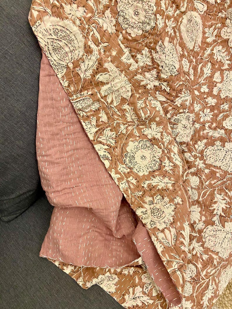 Op de afbeelding: Een gevouwen quilt met een bloemenpatroon in bruin- en cr&egrave;metinten. De achterkant is effen stoffig roze. De quilt is gestikt met witte draad, wat een textuur geeft. Gemaakt van katoen, ideaal voor bed of bank.