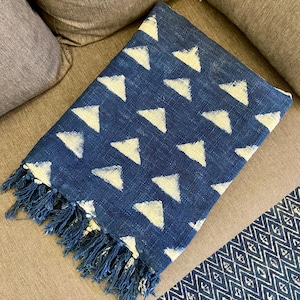 Könnte beinhalten: Eine marineblaue Decke mit einem sich wiederholenden Muster aus weißen Dreiecken. Die Decke hat einen Fransenrand und ist auf einer grauen Oberfläche gefaltet. Ein gemusterter Läufer ist in der unteren rechten Ecke sichtbar.