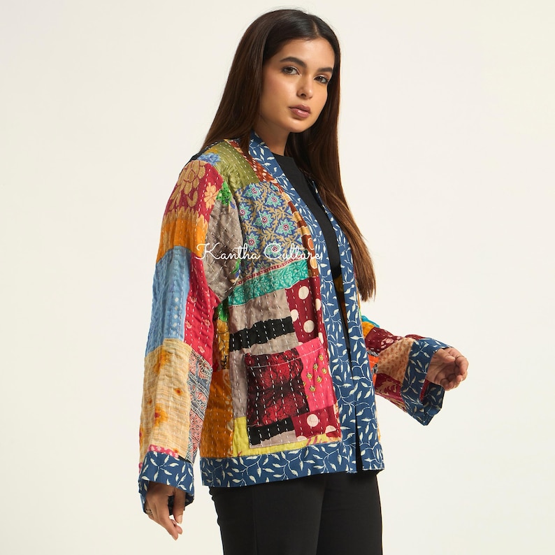 Puede incluir: Una chaqueta de patchwork que presenta una variedad de cuadrados de tela coloridos con patrones intrincados y costuras kantha visibles. La prenda tiene mangas largas, un bolsillo delantero y un borde azul con estampado de hojas blancas. El texto Kantha Collars es visible.
