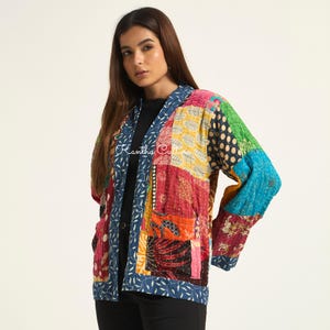 Puede incluir: Una chaqueta de patchwork de manga larga con una variedad de cuadrados de tela coloridos con diversos patrones, incluyendo estampados florales, de lunares y geom&eacute;tricos. La chaqueta tiene un borde con patr&oacute;n de hojas azul y blanco y el texto Kantha Culture.