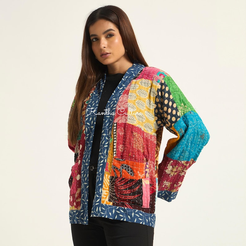 Puede incluir: Una chaqueta de patchwork de manga larga con una variedad de cuadrados de tela coloridos con diversos patrones, incluyendo estampados florales, de lunares y geom&eacute;tricos. La chaqueta tiene un borde con patr&oacute;n de hojas azul y blanco y el texto Kantha Culture.