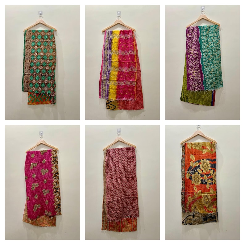 May include: A collection of six colorful, patterned scarves hanging on wooden hangers. The scarves feature various designs, including floral, geometric, and patchwork patterns, in shades of green, pink, orange, and red. Each scarf is made of a soft, lightweight fabric.