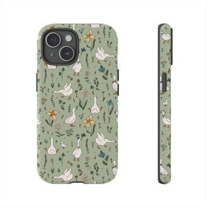 May include: A phone case with a whimsical pattern of white geese, yellow flowers, and green foliage on a sage green background. The case is shown from the front and side, highlighting the wrap-around design and the camera cutout.