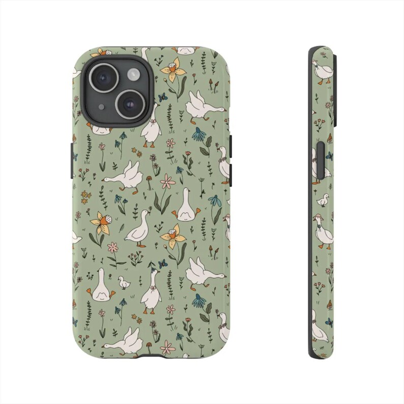 May include: A phone case with a whimsical pattern of white geese, yellow flowers, and green foliage on a sage green background. The case is shown from the front and side, highlighting the wrap-around design and the camera cutout.