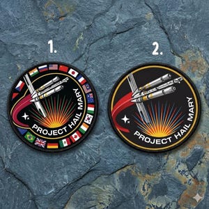 May include: Two circular patches with a black background and a gold border. Each patch features a rocket design with the text "PROJECT HAIL MARY". One patch has flags around the border.