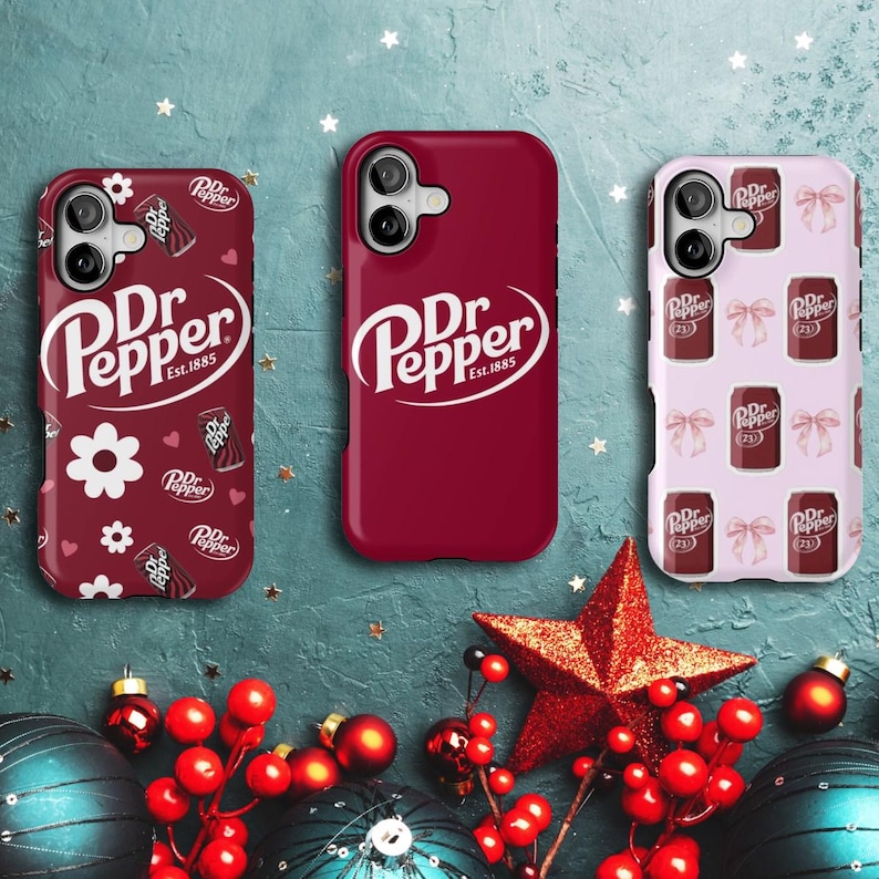 May include: Three phone cases featuring the Dr Pepper logo. One is plain burgundy, another has a pattern of flowers and Dr Pepper cans, and the third has a pattern of bows and Dr Pepper cans. The cases are on a teal background with festive decorations.