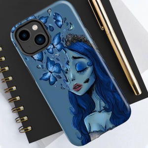 May include: A blue phone case featuring a stylized illustration of a woman with blue skin, closed eyes, and long blue hair. Blue butterflies and floral elements surround her. The case is on a black surface.