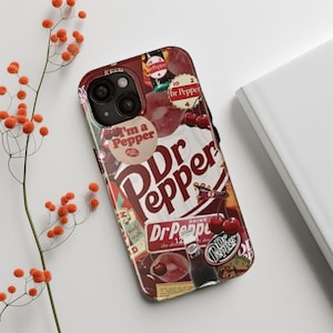 May include: A phone case featuring a collage design with the Dr Pepper logo, cherries, and other vintage-style graphics. The case is predominantly red and white, with the text "I'm a Pepper" visible. The case is on a white surface.