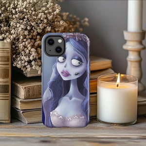 May include: A phone case featuring a cartoon illustration of a blue-skinned woman with long blue hair and a white dress. The case is on a wooden surface with a lit candle and books in the background.