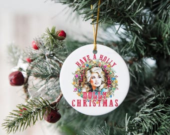 May include: A white ceramic Christmas ornament with a gold string, featuring a portrait of a woman surrounded by a wreath of lights and the text "Have a Holly Dolly Christmas" in red. The ornament hangs on a Christmas tree.
