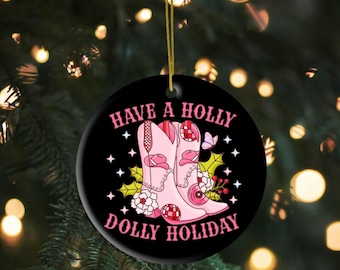 May include: A black round Christmas ornament with the text "Have a Holly Dolly Holiday" in pink. The ornament features pink cowboy boots, stars, and floral accents. A gold string is attached for hanging.