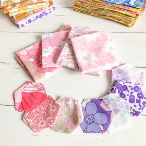 Peut inclure: Un ensemble de chutes de tissu rose et violet avec des motifs floraux. Les chutes sont disposées en cercle sur une surface en bois blanc.