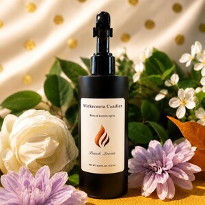 May include: A matte black cylindrical spray bottle with a black trigger nozzle. The white label features the text Wickscentz Candlez, Rose & Lemon Spray, Beach Lovers, and NET WT. 4.06 FL.OZ. / 120 ml, along with a stylized orange flame graphic.