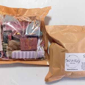 May include: Two brown paper bags, one filled with colorful soap scraps and the other sealed. The bag with soap scraps is transparent, revealing various shapes and colors of soap. The other bag has a label with text.