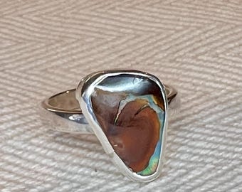 May include: A silver ring with a brown, iridescent, teardrop-shaped stone set in the center.