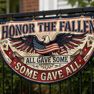 May include: A patriotic banner featuring an eagle and the American flag. The banner displays the text "Honor the Fallen" and "All Gave Some, Some Gave All" in a vintage style. It is attached to a black metal fence.