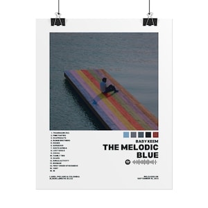 May include: A poster featuring the album art for "The Melodic Blue" by Baby Keem. The image shows a person sitting on a rainbow-colored dock extending into a body of water. The album title and artist name are displayed in bold text.