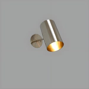 Bring timeless elegance to your interior with this handcrafted Mid-Century Brass Wall Sconce. Inspired by 1950s design, it features clean lines, a satin nickel finish, and soft ambient lighting—perfect for bedrooms, hallways, or reading nooks. Made from solid brass and built to last, this sconce blends vintage charm with modern craftsmanship. Hardwired with E12/E14 socket. Bulb not included.