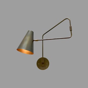 May include: A brass-toned wall sconce with a conical shade and an adjustable arm. The shade has a warm, golden interior. The sconce is mounted on a round base, and the arm extends to the side.