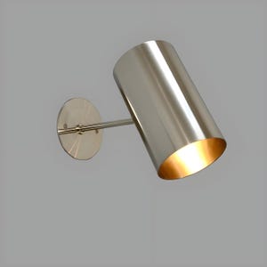 Bring timeless elegance to your interior with this handcrafted Mid-Century Brass Wall Sconce. Inspired by 1950s design, it features clean lines, a satin nickel finish, and soft ambient lighting—perfect for bedrooms, hallways, or reading nooks. Made from solid brass and built to last, this sconce blends vintage charm with modern craftsmanship. Hardwired with E12/E14 socket. Bulb not included.