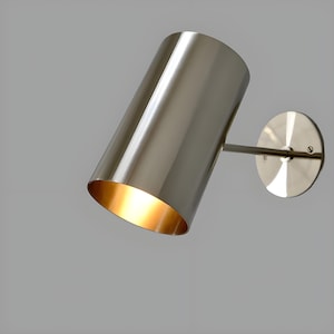Bring timeless elegance to your interior with this handcrafted Mid-Century Brass Wall Sconce. Inspired by 1950s design, it features clean lines, a satin nickel finish, and soft ambient lighting—perfect for bedrooms, hallways, or reading nooks. Made from solid brass and built to last, this sconce blends vintage charm with modern craftsmanship. Hardwired with E12/E14 socket. Bulb not included.