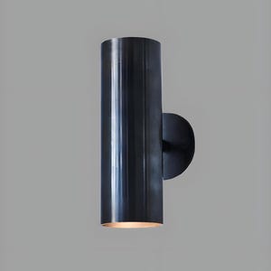 Peut inclure: Applique murale cylindrique moderne, finition métallique foncée. Le corps tubulaire vertical est fixé à une plaque circulaire. La lumière émane du bas du tube, créant une lueur chaleureuse. Design minimaliste.