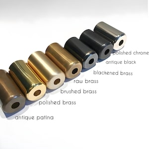 Op de afbeelding: Een verzameling cilindrische metalen objecten in verschillende afwerkingen, waaronder gepolijst chroom, antiek zwart en zwart gemaakt messing. Andere afwerkingen zijn onbewerkt messing, geborsteld messing, gepolijst messing en antieke patina. Elk object heeft een gat aan &eacute;&eacute;n uiteinde.
