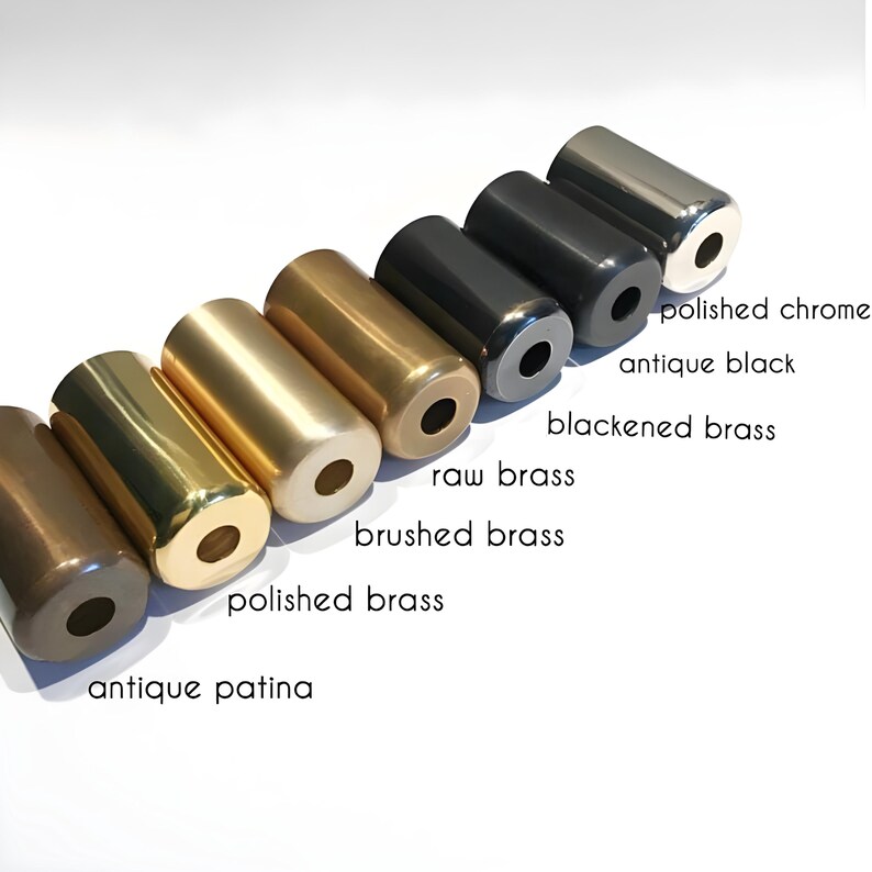 Op de afbeelding: Een verzameling cilindrische metalen objecten in verschillende afwerkingen, waaronder gepolijst chroom, antiek zwart en zwart gemaakt messing. Andere afwerkingen zijn onbewerkt messing, geborsteld messing, gepolijst messing en antieke patina. Elk object heeft een gat aan &eacute;&eacute;n uiteinde.