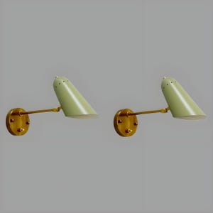 Könnte beinhalten: Zwei Wandleuchten im Mid-Century-Modern-Stil. Jede Leuchte hat einen hellgrünen, konisch geformten Schirm, einen messingfarbenen Arm und eine runde messingfarbene Basis. Die Schirme haben kleine Belüftungslöcher. Die Leuchten sind auf grauem Hintergrund montiert.