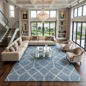 Hand tufted wool area rug with a prominent white geometric diamond pattern on a textured slate blue background. The handmade carpet is laid flat on a dark hardwood floor in a luxury living room, partially styled under a cream-colored sectional sofa and glass coffee table, capturing the complete pattern and premium texture.