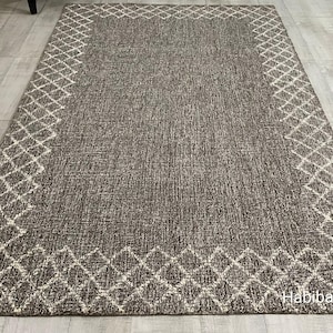 May include: A rectangular, gray rug with a white diamond pattern border. The rug has a textured appearance and is placed on a light-colored tiled floor. The text "Habiba Rugs Art" is visible in the bottom right corner.