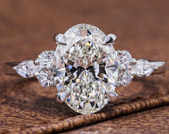 May include: A silver-toned ring featuring a large, central oval-cut clear gemstone held by four prongs. The band is accented on each side by a cluster of three smaller round-cut stones and one pear-cut stone, all set in a polished metal band.