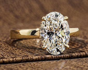 May include: A gold ring featuring a large, oval-cut, clear faceted gemstone set in a four-prong mounting. The band is smooth and polished, showcasing a classic design with a prominent center stone that reflects light across its many surfaces.
