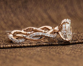 May include: A rose gold ring featuring a twisted band encrusted with small clear stones. The center setting holds a large, clear, oval-shaped stone surrounded by a halo of smaller clear stones. The text THEHOUSEOFADGROWN is visible on the band.