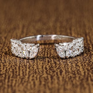 May include: A silver-toned open ring featuring two clusters of marquise-cut clear stones on each end. The band is polished and metallic, with the stones arranged in a symmetrical pattern that leaves a gap at the front of the ring design.