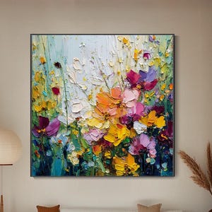 Puede incluir: Un cuadro cuadrado sobre lienzo que presenta un vibrante arreglo floral con pinceladas empastadas, gruesas y texturizadas en tonos amarillo, naranja, rosa, morado y verde sobre un fondo claro y neutro, expuesto en una pared blanca.
