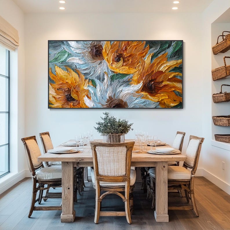 May include: A large framed painting of sunflowers in shades of yellow, orange, white, and brown. The painting is displayed above a wooden dining table with six chairs. A small potted plant sits on the table.
