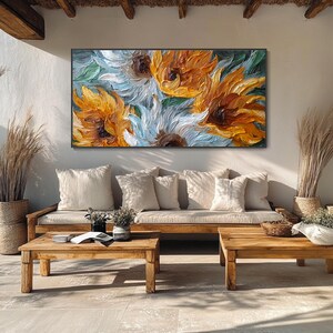May include: A large, framed oil painting of sunflowers in shades of yellow, orange, and white. The artwork hangs above a wooden sofa with cream-colored pillows. Two wooden coffee tables sit in front of the sofa, creating a cozy outdoor living space.