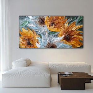 May include: An oil painting of sunflowers in shades of yellow, orange, and white, with green leaves. The artwork is displayed in a black frame, adding a touch of elegance. The painting's textured brushstrokes create a sense of depth and movement, making it a striking piece of wall art.