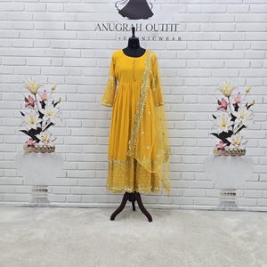 May include: A mustard yellow long-sleeved dress with a round neckline and a row of small buttons down the centre chest. The dress features intricate gold embroidery along the hem and sleeves, paired with a matching sheer yellow dupatta with gold trim.
