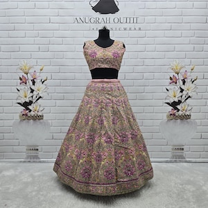 May include: A two-piece formal outfit on a mannequin. The outfit features a sleeveless, pink embroidered top and a matching full skirt. The skirt and top are adorned with intricate floral patterns in shades of pink, gold, and purple. The brand name "ANUGRAH OUTFIT" is visible.