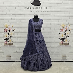 Peut inclure: Une tenue ethnique bleu marine, comprenant un haut, une jupe et une écharpe transparente. La tenue est ornée de motifs complexes et de paillettes. La marque "ANUGRAH OUTFIT" est affichée au-dessus.