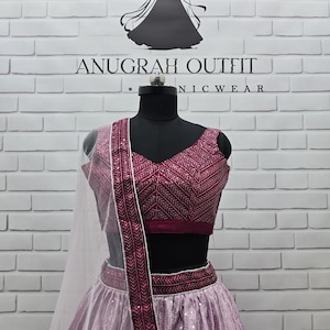 May include: A formal, two-piece outfit on a mannequin. The top is a deep magenta with intricate embroidery, paired with a matching skirt. The skirt has a sequined design. A sheer, white scarf is draped over the shoulder. The text "ANUGRAH OUTFIT NICWEAR" is visible.