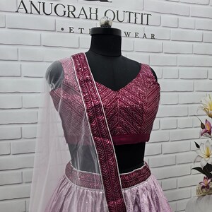 May include: A formal outfit displayed on a mannequin. The ensemble features a magenta-colored top and skirt, with intricate patterns and embellishments. A sheer, white scarf drapes over the shoulder. The brand name "ANUGRAH OUTFIT" is visible in the background.