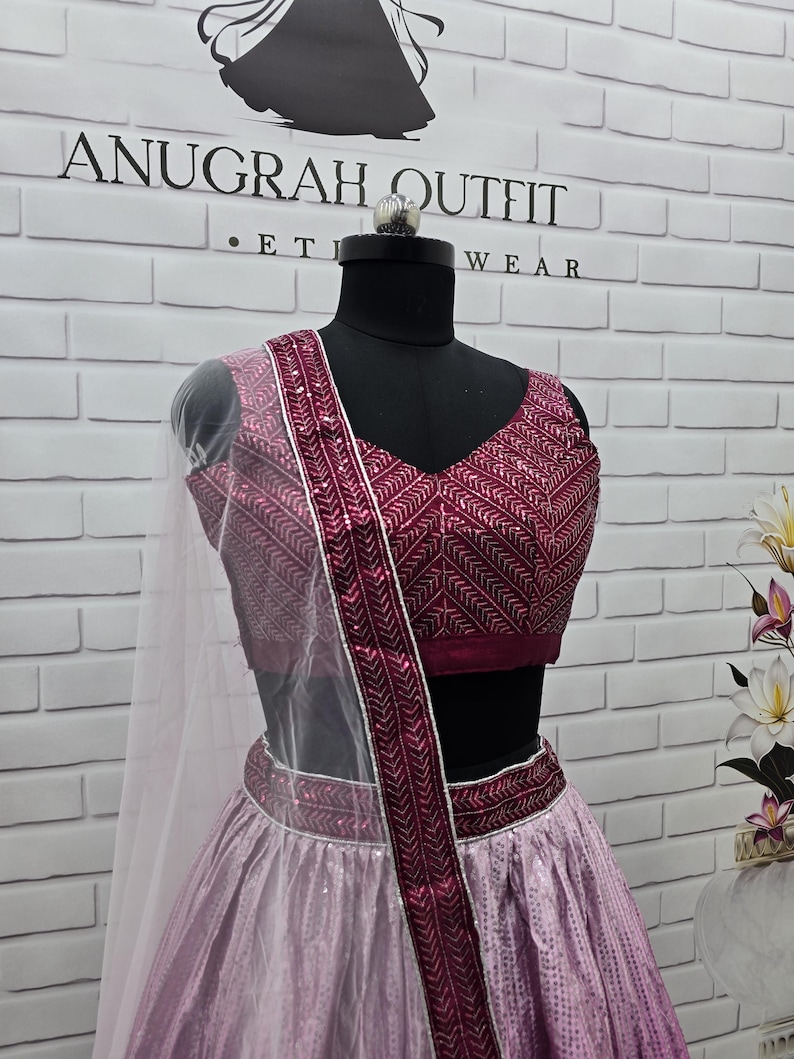 May include: A formal outfit displayed on a mannequin. The ensemble features a magenta-colored top and skirt, with intricate patterns and embellishments. A sheer, white scarf drapes over the shoulder. The brand name "ANUGRAH OUTFIT" is visible in the background.