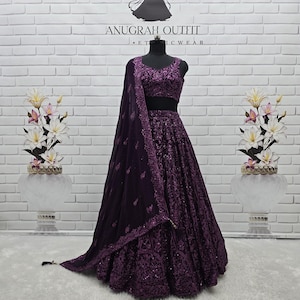 Puede incluir: Un vestido de noche morado oscuro con intrincados detalles de lentejuelas y bordados. El conjunto incluye un top corto sin mangas, una falda completa y un chal transparente a juego. El texto "ANUGRAH OUTFIT" es visible en la pared.