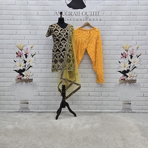 May include: A dark brown tunic with short sleeves and gold embroidery, paired with bright yellow pleated trousers featuring small mirror accents and a matching sheer yellow dupatta with a gold border, displayed on a mannequin.